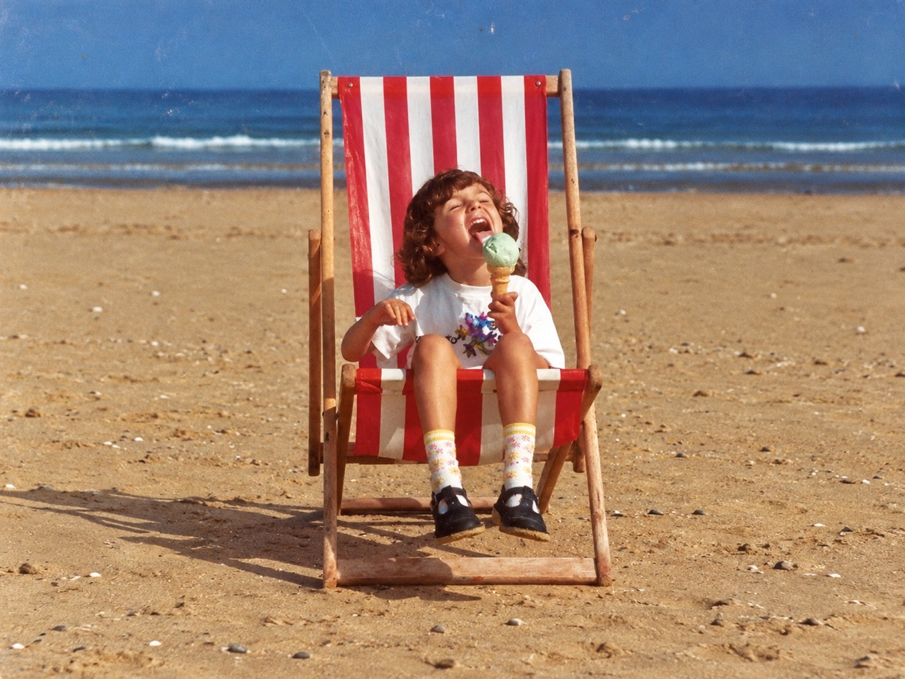 Bambini — child enjoying an ice cream in a striped deckchair on the beach