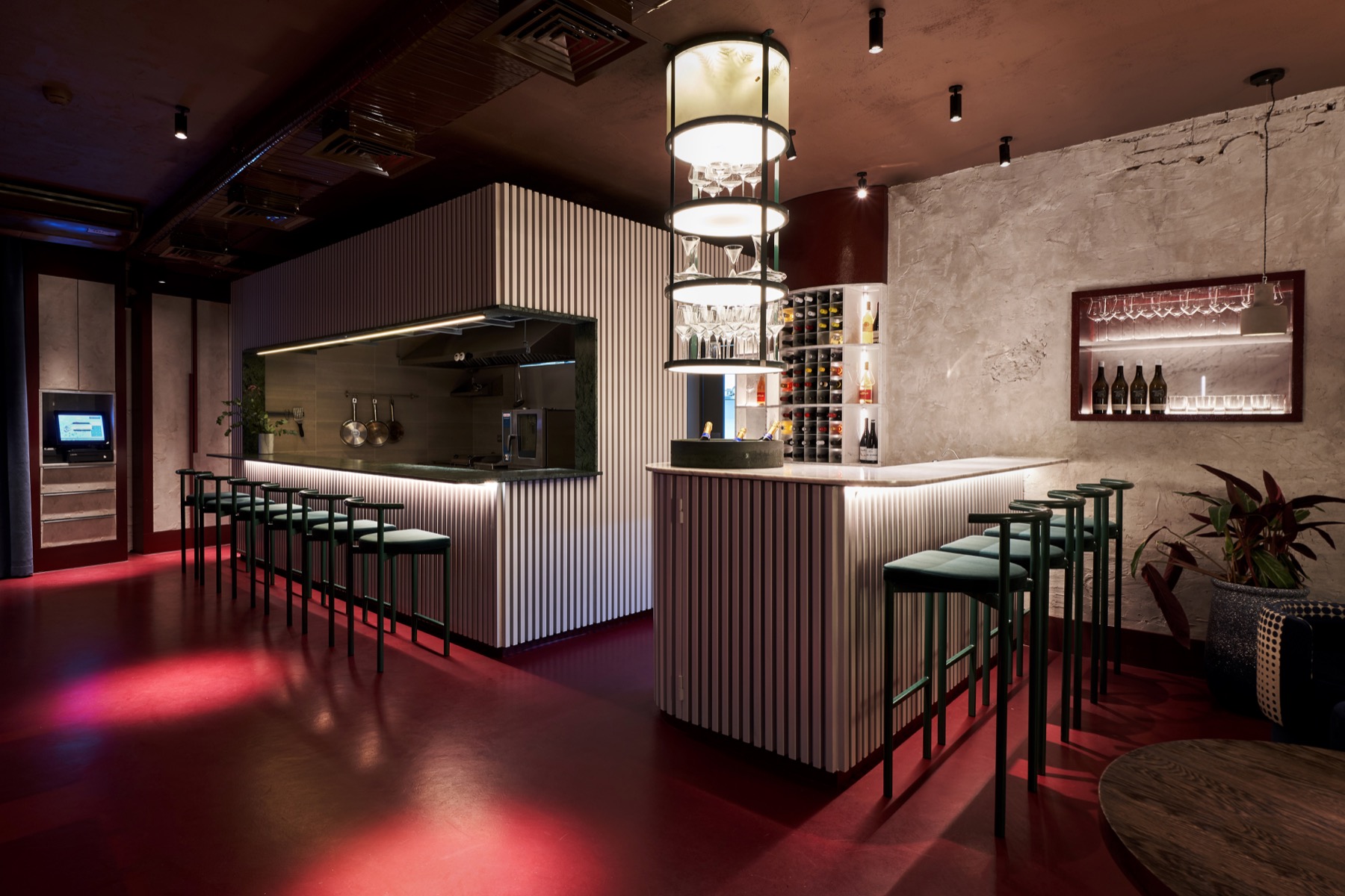 Commons — open kitchen and bar with ribbed counters, green stools and a red floor
